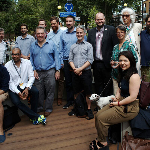 A group of people dressed in business casual attire, and a small dog, stand and sit in a group, smiling at the camera.