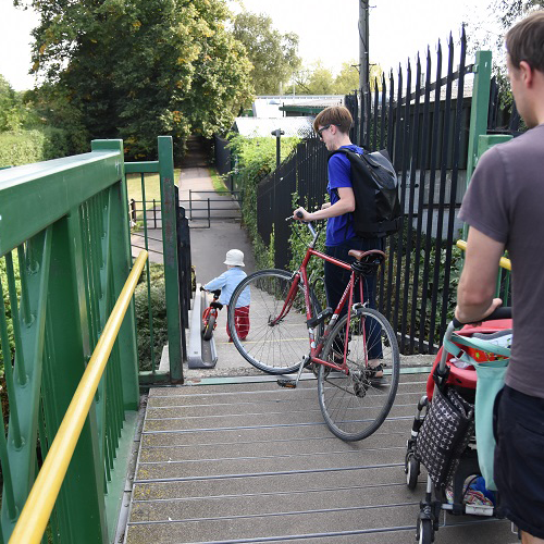 Three people walk down an outdoor staircase, two wheeling bikes and one with a pram.