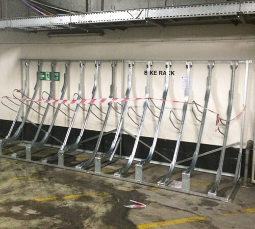 Empty bike storage racks inside an underground carpark, with red striped tape around them.